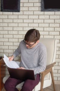 man with laptop sitting on an armchair while reading a document